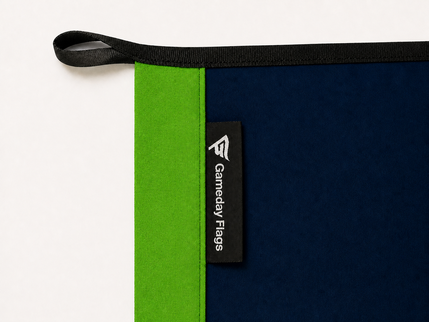Authentic Gameday Flag construction detail showing the full Action Green header, navy face, black upper loop and perimeter webbing, stitching, and woven Gameday Flags tag.