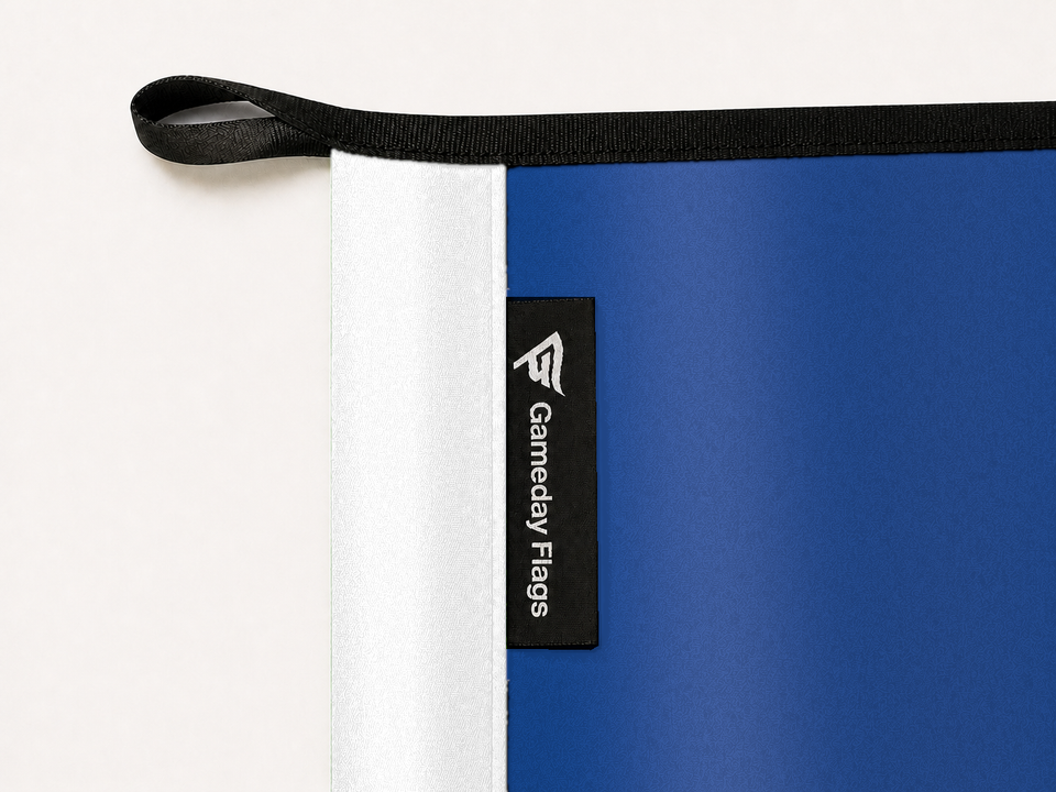 United States Air Force Flag Authentic Gameday Flag construction detail — restrained woven-satin White Header sewn header, textured Air Force Blue Field face, crisp woven Gameday Flags tag and controlled contact shadow, black loop, perimeter webbing, and stitching — source_sha256=9c383aed2eb76f7e4a51d77f978abee3eb9ee86bd8782c059ad59923e0539124