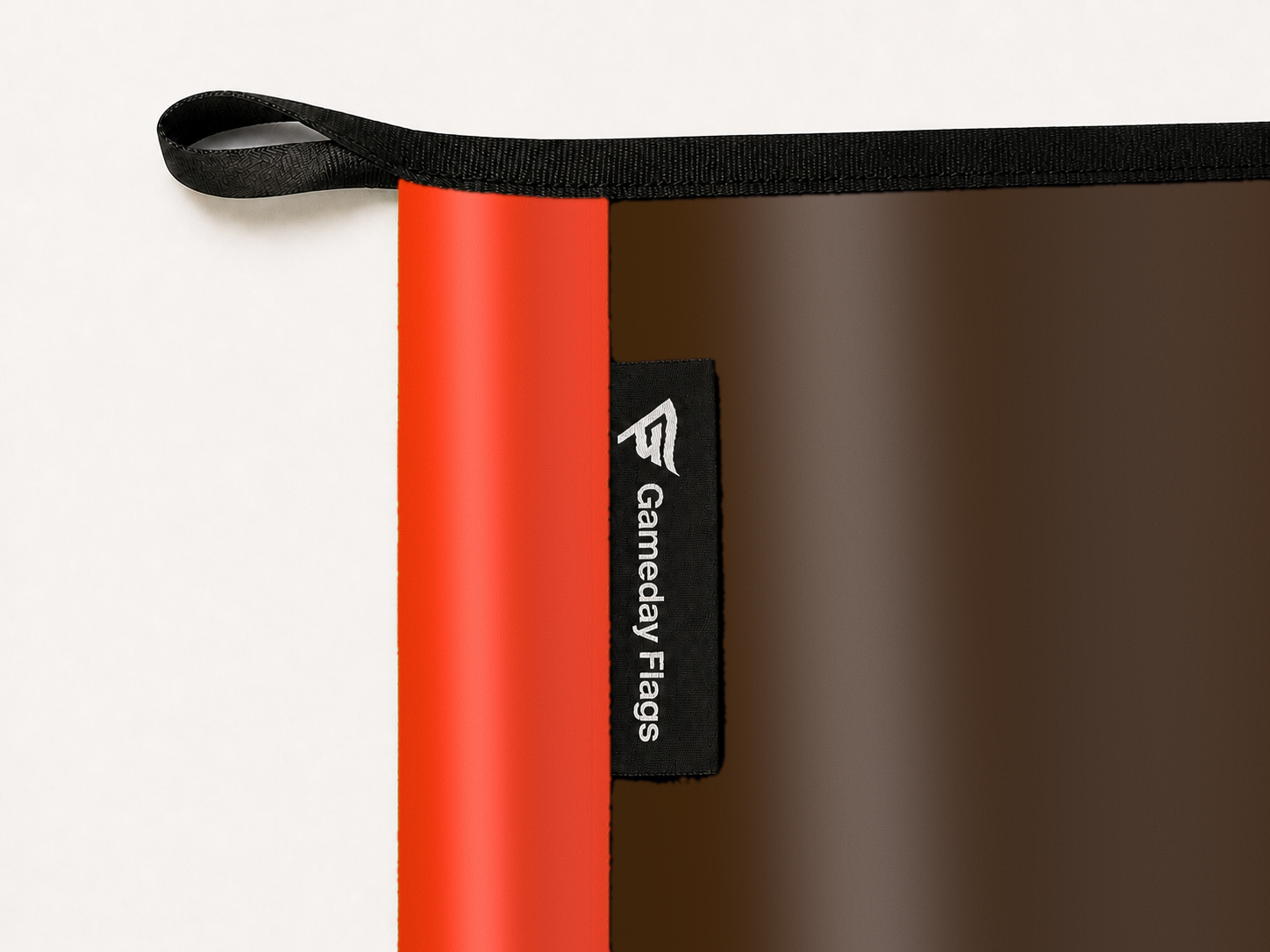 Cleveland Browns Authentic Gameday Flag construction detail — restrained woven-satin Cleveland Browns Accent sewn header, textured Cleveland Browns Primary face, woven Gameday Flags tag, black loop, perimeter webbing, and stitching — source_sha256=73b462eaa4721198ce6dc852c92cce703bd1e8a8afc30f3ab299309b4246ff26