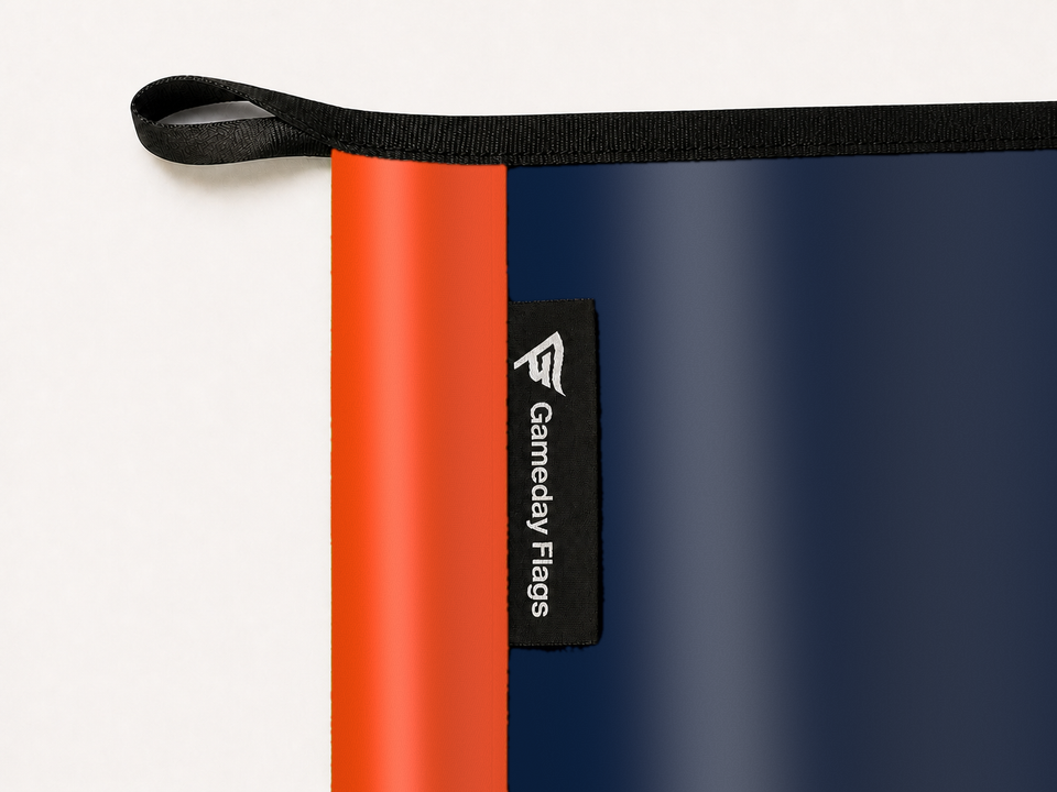 Denver Broncos Authentic Gameday Flag construction detail — restrained woven-satin Denver Broncos Accent sewn header, textured Denver Broncos Primary face, woven Gameday Flags tag, black loop, perimeter webbing, and stitching — source_sha256=bf92624c0d7cfe3d1187378017afade0a345b1477599aa2bab22bd56ad46f827