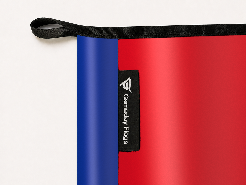 Arsenal Authentic Gameday Flag construction detail — restrained woven-satin Arsenal Accent sewn header, textured Arsenal Primary face, woven Gameday Flags tag, black loop, perimeter webbing, and stitching — source_sha256=9b829c554ccec2cea32e245b23b7986fb381d23fdd949aff444699273fd0fd31