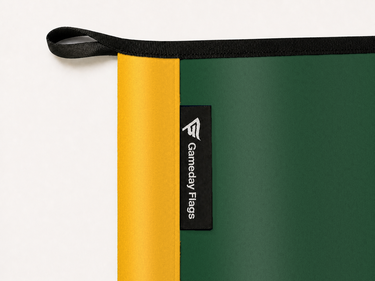 Green Bay Packers Authentic Gameday Flag construction detail — restrained woven-satin Green Bay Packers Accent sewn header, textured Green Bay Packers Primary face, crisp woven Gameday Flags tag and controlled contact shadow, black loop, perimeter webbing, and stitching — source_sha256=d682f1f78b4f2c4f14826c7dfd835e2933dfdee3771f51dd2fb934ae022d1282