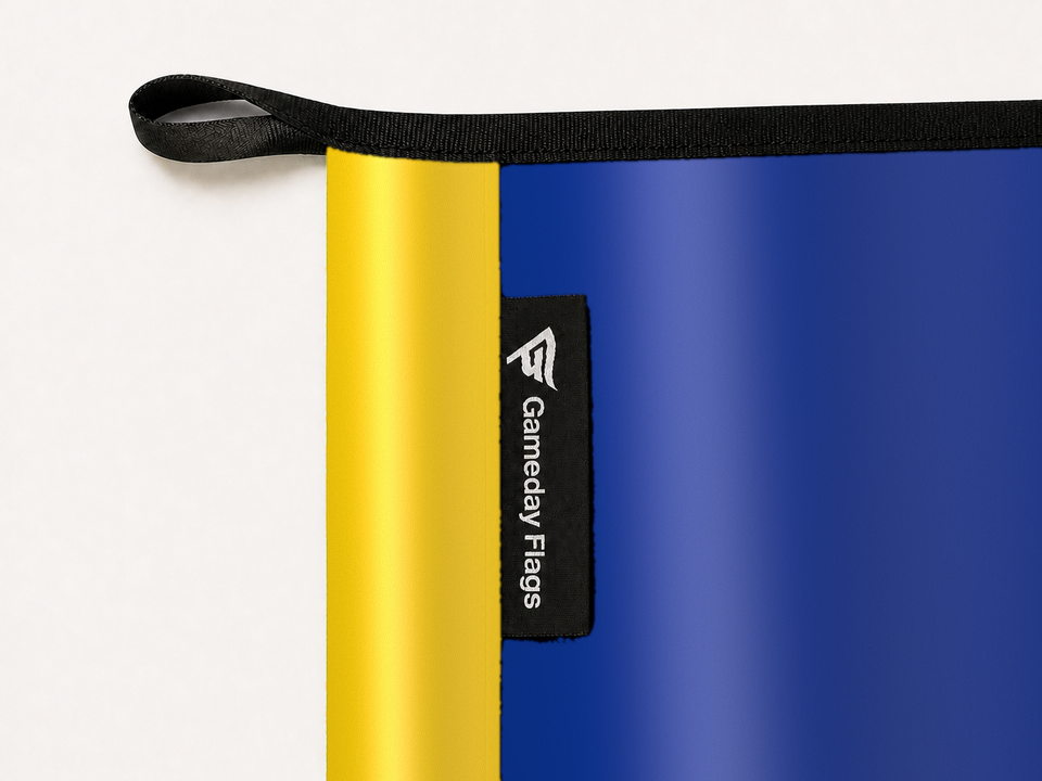 Los Angeles Rams Authentic Gameday Flag construction detail — restrained woven-satin Los Angeles Rams Accent sewn header, textured Los Angeles Rams Primary face, woven Gameday Flags tag, black loop, perimeter webbing, and stitching — source_sha256=27d26b81a1e0248aeb52cb2068e00f2d848d68b3e900352a8a973014458f92cb
