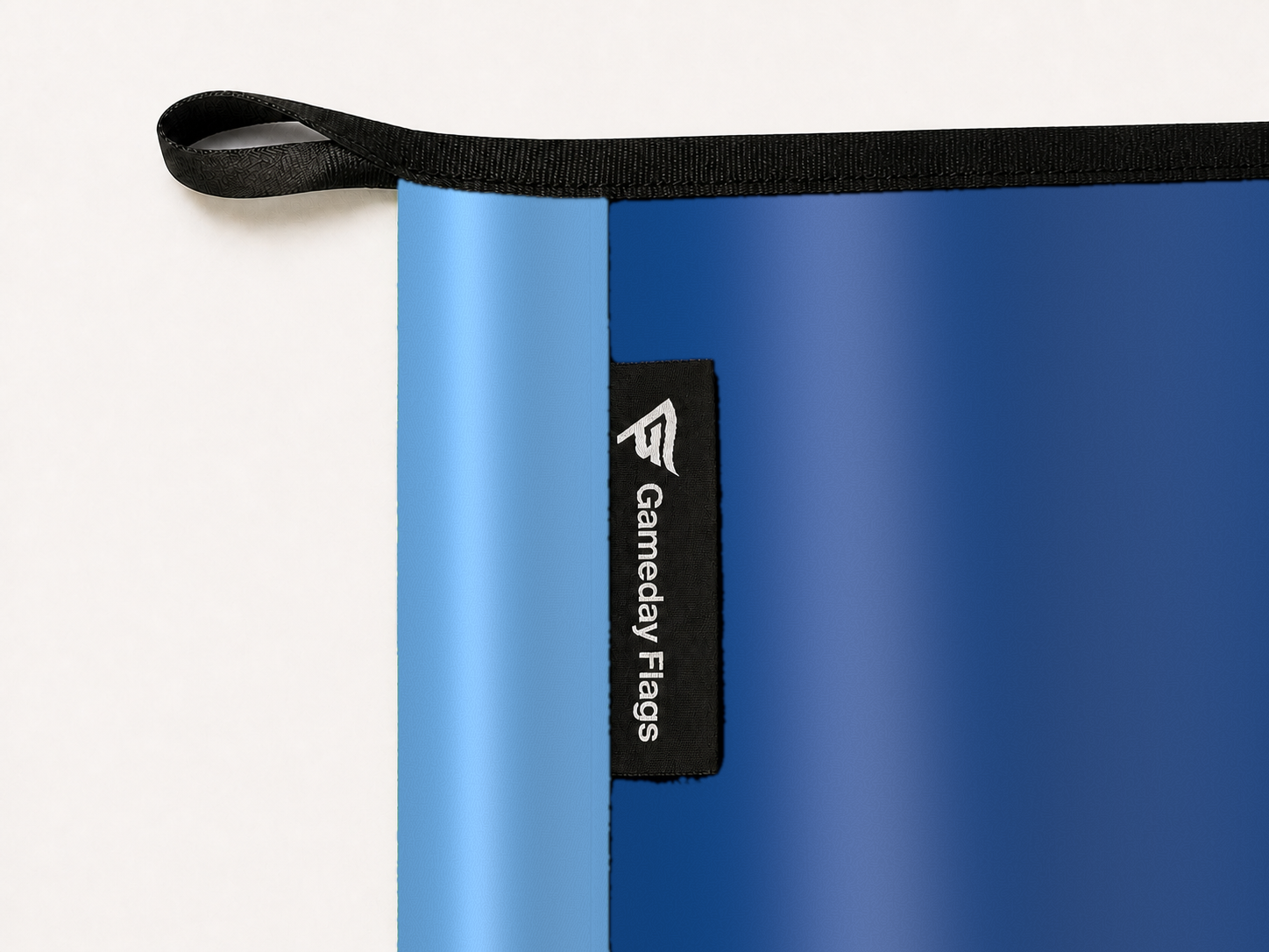 Toronto Blue Jays Authentic Gameday Flag construction detail — restrained woven-satin Toronto Blue Jays Accent sewn header, textured Toronto Blue Jays Primary face, woven Gameday Flags tag, black loop, perimeter webbing, and stitching — source_sha256=a6e1afb7b6235ed5693c351305780f671966da615541f7e5f77eece05a48ce18