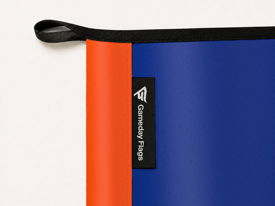 FC Cincinnati Authentic Gameday Flag construction detail — restrained woven-satin FC Cincinnati Accent sewn header, textured FC Cincinnati Primary face, crisp woven Gameday Flags tag and controlled contact shadow, black loop, perimeter webbing, and stitching — source_sha256=9903c26d12e93710384ef5e8fcdf1341599a7c223a9d88a13ce7d1951709e61c