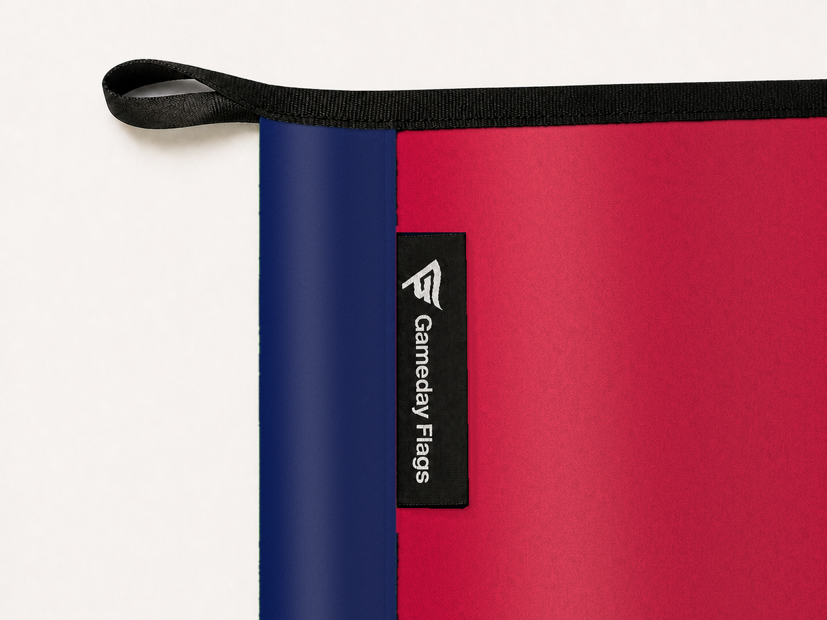 FC Dallas Authentic Gameday Flag construction detail — restrained woven-satin FC Dallas Accent sewn header, textured FC Dallas Primary face, crisp woven Gameday Flags tag and controlled contact shadow, black loop, perimeter webbing, and stitching — source_sha256=f2cef4100a6152728a296a5fd5a12478cbae1f8eaa891e8f325303bd46ef0f67