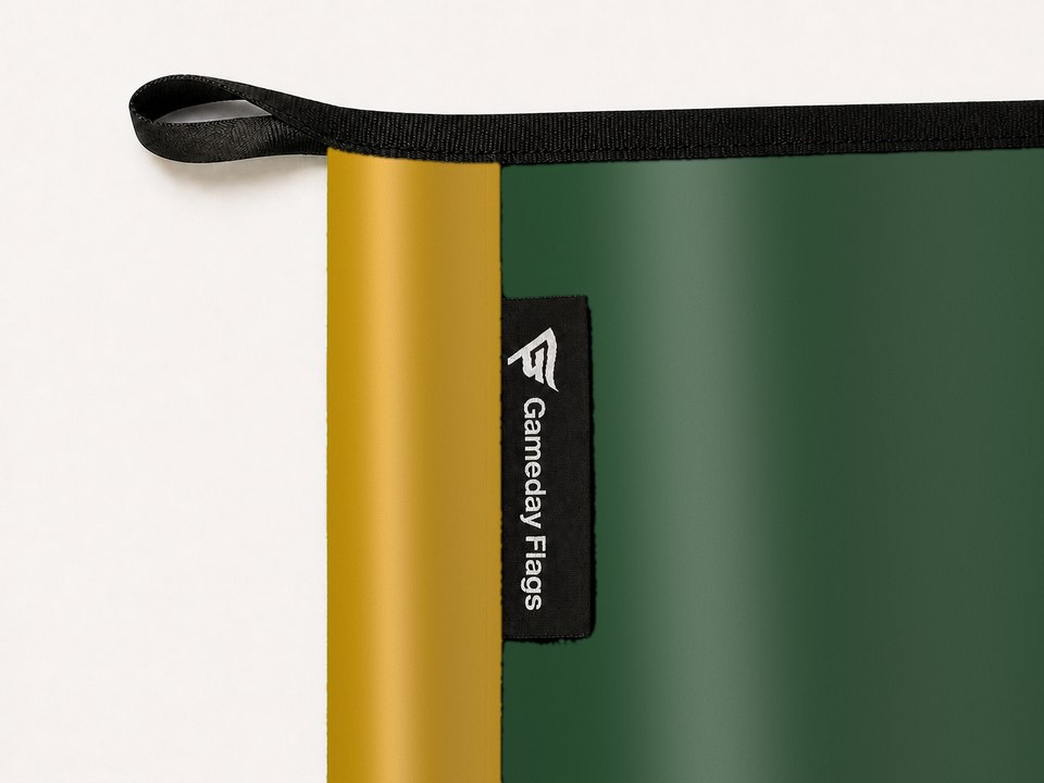 Portland Timbers Authentic Gameday Flag construction detail — restrained woven-satin Portland Timbers Accent sewn header, textured Portland Timbers Primary face, woven Gameday Flags tag, black loop, perimeter webbing, and stitching — source_sha256=39e420965bc91d42b2671a0278497c60db71e1c58600050c5966130e66061549