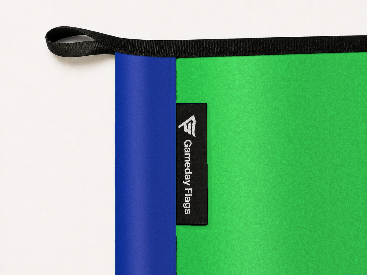 Seattle Sounders FC Authentic Gameday Flag construction detail — restrained woven-satin Seattle Sounders FC Accent sewn header, textured Seattle Sounders FC Primary face, crisp woven Gameday Flags tag and controlled contact shadow, black loop, perimeter webbing, and stitching — source_sha256=ba36ca4841dec0a53391b5c5d2698e828899a62178d45fd2e55d632741fc7ff1