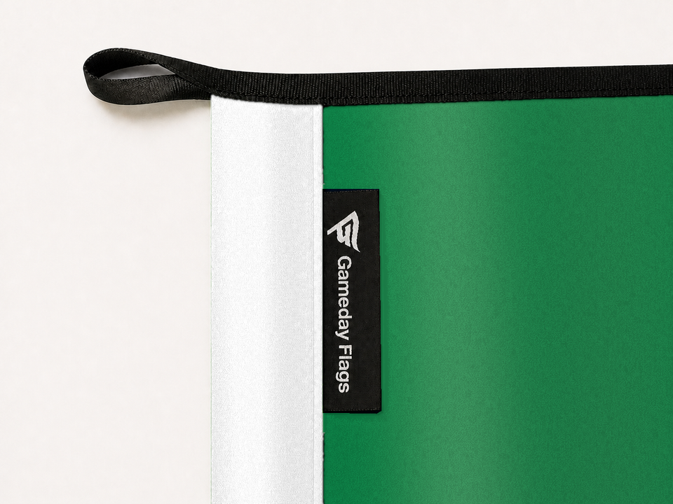 Boston Celtics Authentic Gameday Flag construction detail — restrained woven-satin Boston Celtics Accent sewn header, textured Boston Celtics Primary face, crisp woven Gameday Flags tag and controlled contact shadow, black loop, perimeter webbing, and stitching — source_sha256=5327bdac7f53e81a82464557477df1c74bf850ebcbd6feb64ed2eddefc34cdfe