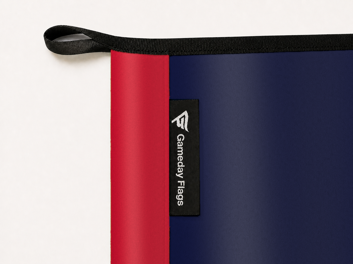 LA Clippers Authentic Gameday Flag construction detail — restrained woven-satin LA Clippers Accent sewn header, textured LA Clippers Primary face, crisp woven Gameday Flags tag and controlled contact shadow, black loop, perimeter webbing, and stitching — source_sha256=f1f164bd2e7e1b45f726f0959544b2da633833b13736380badb70fffc4e96fae