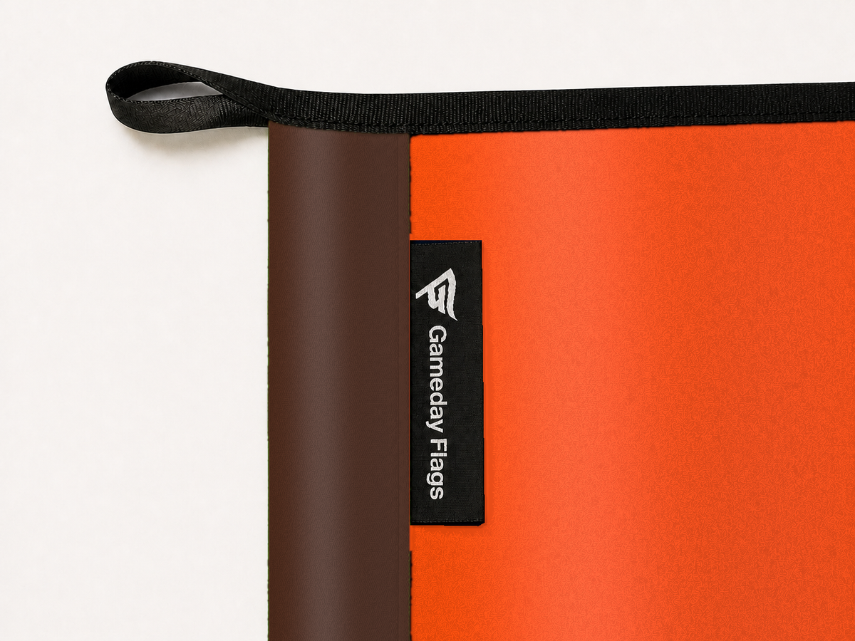 Bowling Green Falcons Authentic Gameday Flag construction detail — restrained woven-satin Bowling Green Falcons Accent sewn header, textured Bowling Green Falcons Primary face, crisp woven Gameday Flags tag and controlled contact shadow, black loop, perimeter webbing, and stitching — source_sha256=fd37f0e4a2f0976e93c3b3e554699ea7fba2f02d68dc31ad04dd60f019faa573