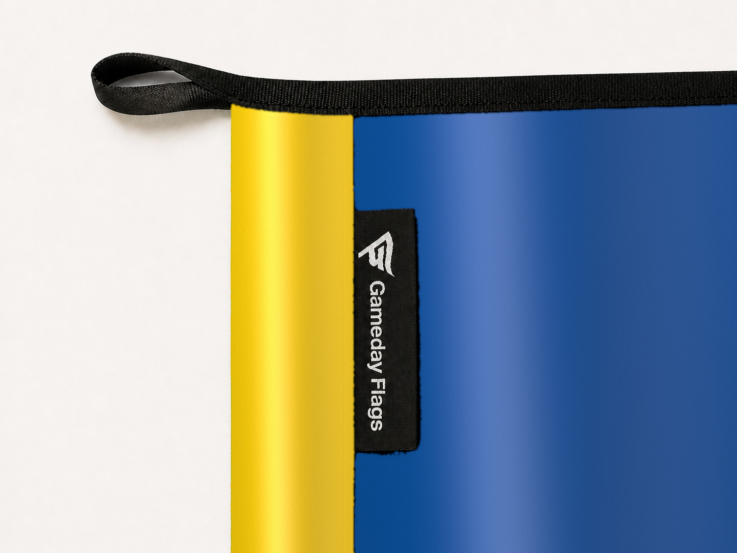 Delaware Blue Hens Authentic Gameday Flag construction detail — restrained woven-satin Delaware Blue Hens Accent sewn header, textured Delaware Blue Hens Primary face, woven Gameday Flags tag, black loop, perimeter webbing, and stitching — source_sha256=bf70f39790f98c873e14c8664ecee9aac8d7dc3a1c0e402c46daad24f9bfd634