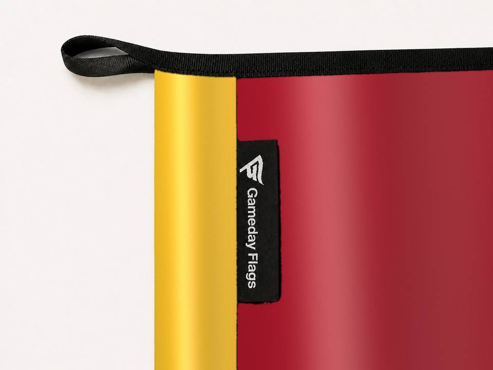 Iowa State Cyclones Authentic Gameday Flag construction detail — restrained woven-satin Iowa State Cyclones Accent sewn header, textured Iowa State Cyclones Primary face, woven Gameday Flags tag, black loop, perimeter webbing, and stitching — source_sha256=bd5e06aa1c697f5b254d22b073e861201ed93579397911e8bd27df0a02c905f2