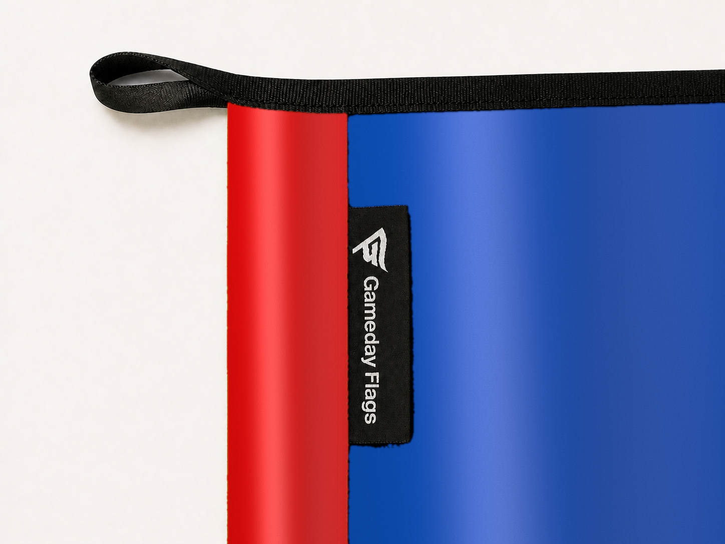 Kansas Jayhawks Authentic Gameday Flag construction detail — restrained woven-satin Kansas Jayhawks Accent sewn header, textured Kansas Jayhawks Primary face, woven Gameday Flags tag, black loop, perimeter webbing, and stitching — source_sha256=dd15f64d8ccc85a4b494f22f5b28c37e9427ae8d79f26935d599da2b5c09b8d9