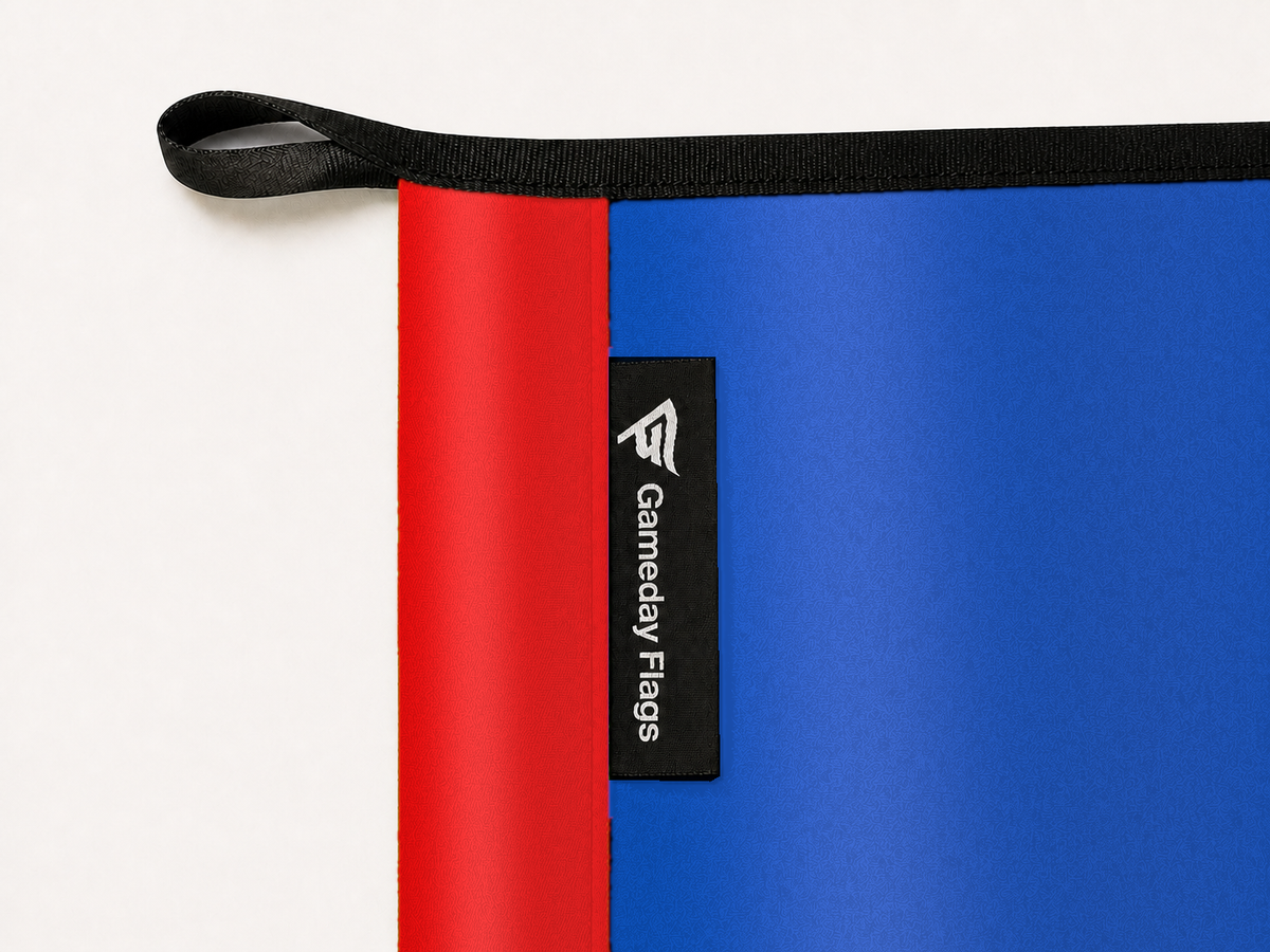 Kansas Jayhawks Authentic Gameday Flag construction detail — restrained woven-satin Kansas Jayhawks Accent sewn header, textured Kansas Jayhawks Primary face, crisp woven Gameday Flags tag and controlled contact shadow, black loop, perimeter webbing, and stitching — source_sha256=bf3bee134a86faec7cf38b44e60dd7a2419db6a1b99f703b8f5f5033af5f3584