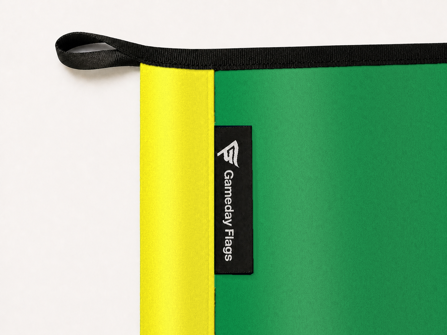 Oregon Ducks Authentic Gameday Flag construction detail — restrained woven-satin Oregon Yellow sewn header, textured Oregon Green face, crisp woven Gameday Flags tag and controlled contact shadow, black loop, perimeter webbing, and stitching — source_sha256=414a366edda35ccdf70816a86553bd413add92a3de2ebc7f8294adb251ffdc46