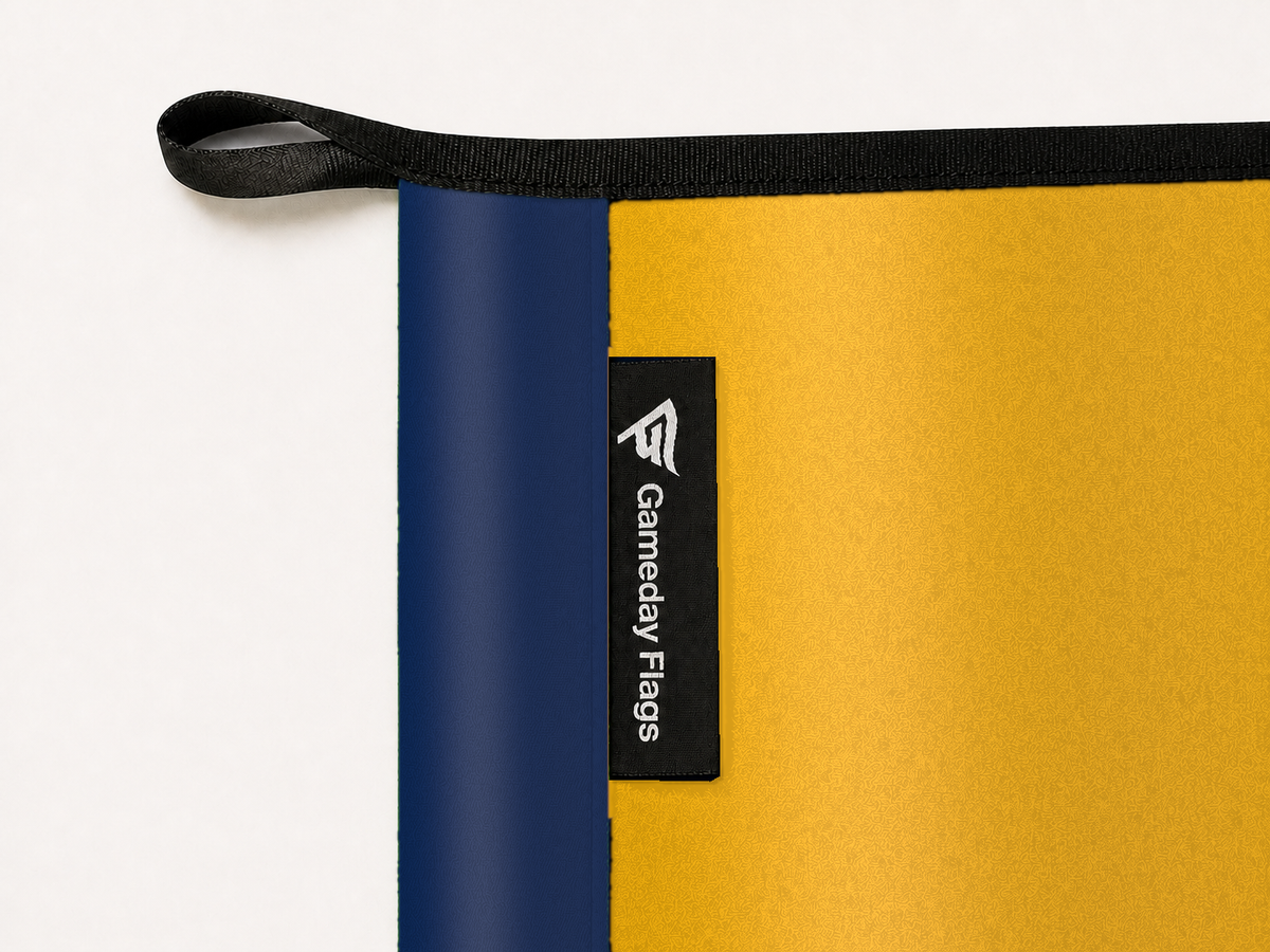West Virginia Mountaineers Authentic Gameday Flag construction detail — restrained woven-satin West Virginia Mountaineers Accent sewn header, textured West Virginia Mountaineers Primary face, crisp woven Gameday Flags tag and controlled contact shadow, black loop, perimeter webbing, and stitching — source_sha256=c10d219dc862ac4512d2965b6b4ca3281811c2916e9aac554ad9a6ffe9564a90
