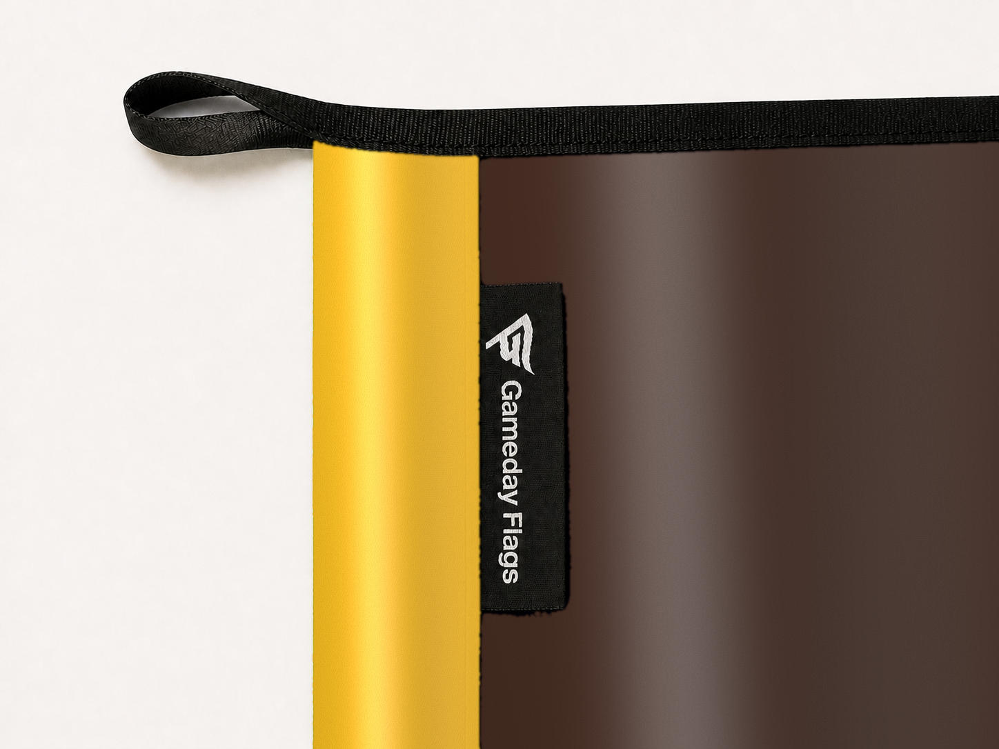 Wyoming Cowboys Authentic Gameday Flag construction detail — restrained woven-satin Wyoming Cowboys Accent sewn header, textured Wyoming Cowboys Primary face, woven Gameday Flags tag, black loop, perimeter webbing, and stitching — source_sha256=cca8be261eaea89e63ea39f1811bbbd43eb7a3e9012ba093c18b416b428c0b6a