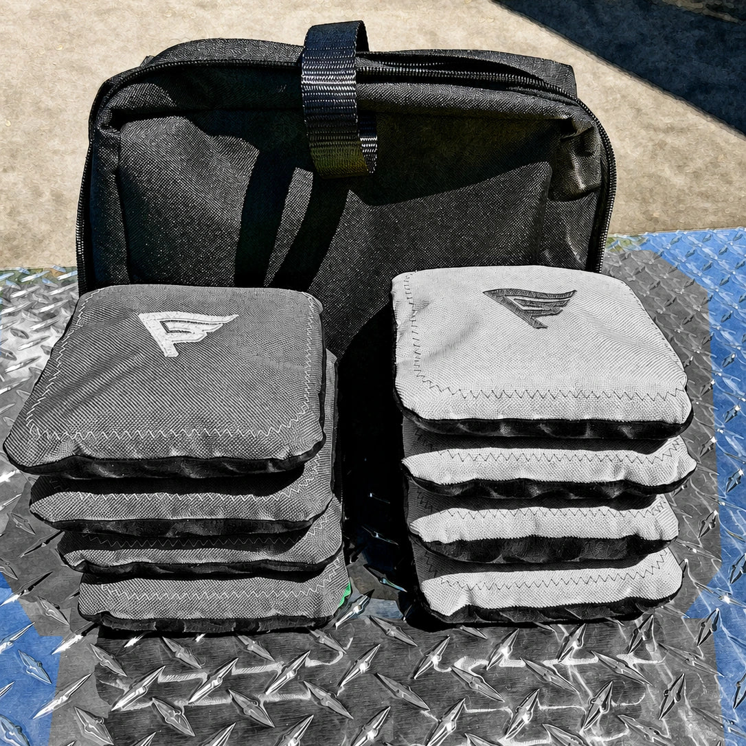 Two stacks of Gameday cornhole bags and their black carry case on diamond plate