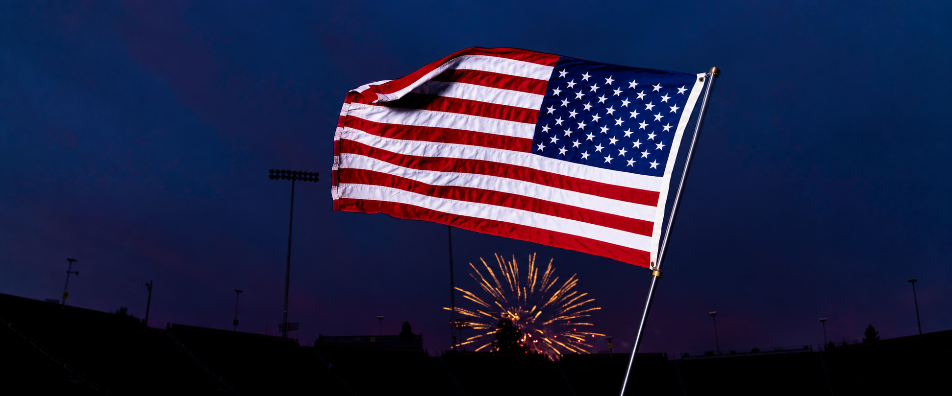 American flag flying from an MVP pole against a twilight sky and fireworks