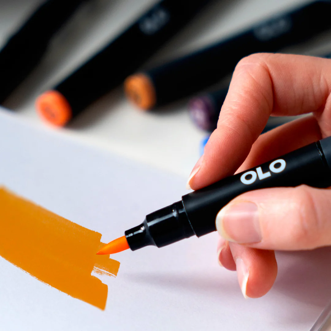 An OLO brush marker making an orange stroke on white drawing paper